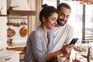 Couple drinking coffee and using cell phone during breakfast in kitchen at home
